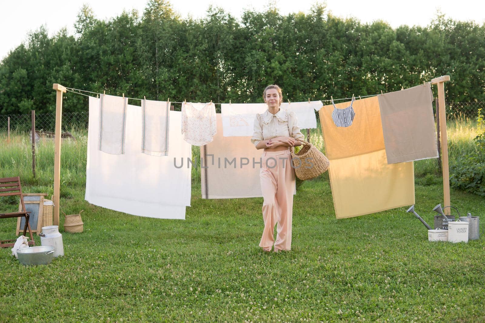 Laundry day. A woman hangs linen and towels on a tree in the courtyard of a village house. Summer cottage concept.