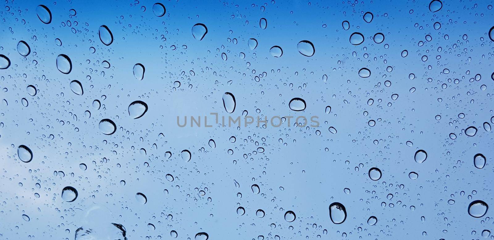 Water droplets perspective through window glass surface against blue sky good for multimedia content backgrounds