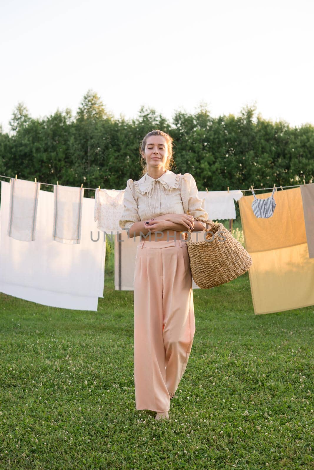 Laundry day. A woman hangs linen and towels on a tree in the courtyard of a village house. Summer cottage concept.