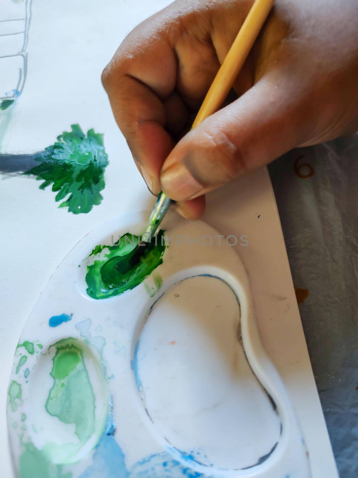 A child is painting in a paper. In the picture the child is painting grasses in a white background.