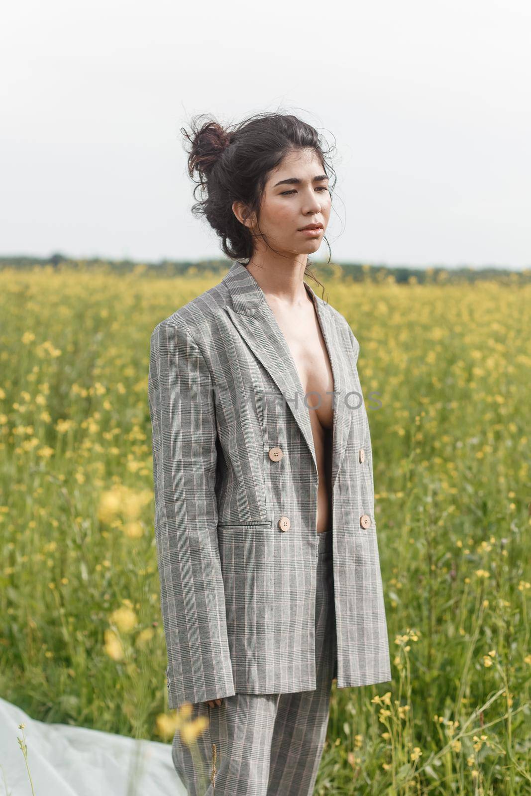 An Asian model poses in a field of yellow flowers for a clothing brand, polyethylene is the main props for a photo shoot. The concept of manufacturing clothing from recycled plastic. A woman in a pantsuit is standing on a plastic bag.