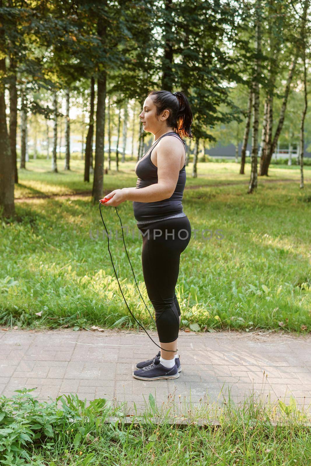 A charming brunette woman plus-size body positive practices sports in nature.