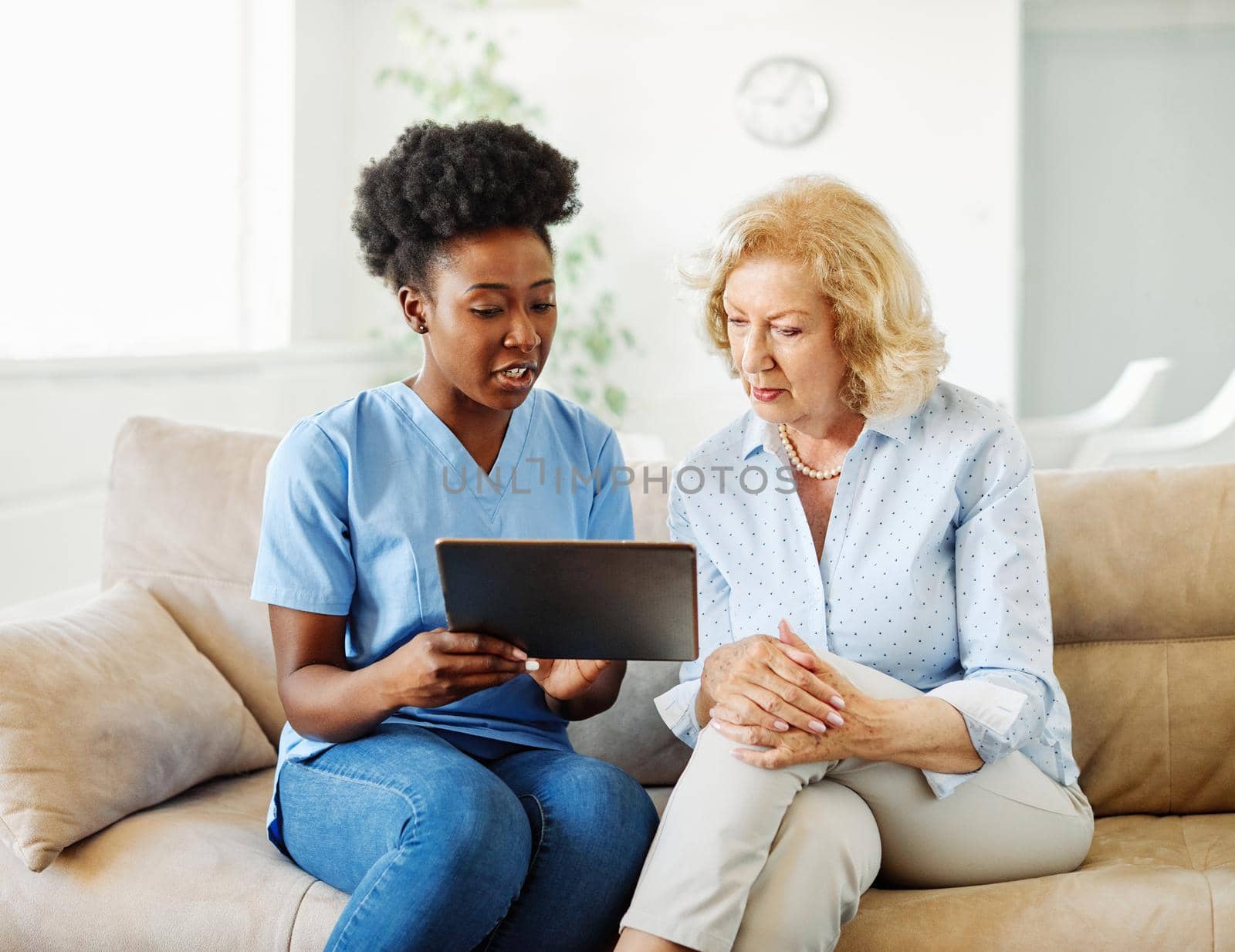 Doctor or nurse caregiver showing a tablet screen to senior woman and laughing at home or nursing home