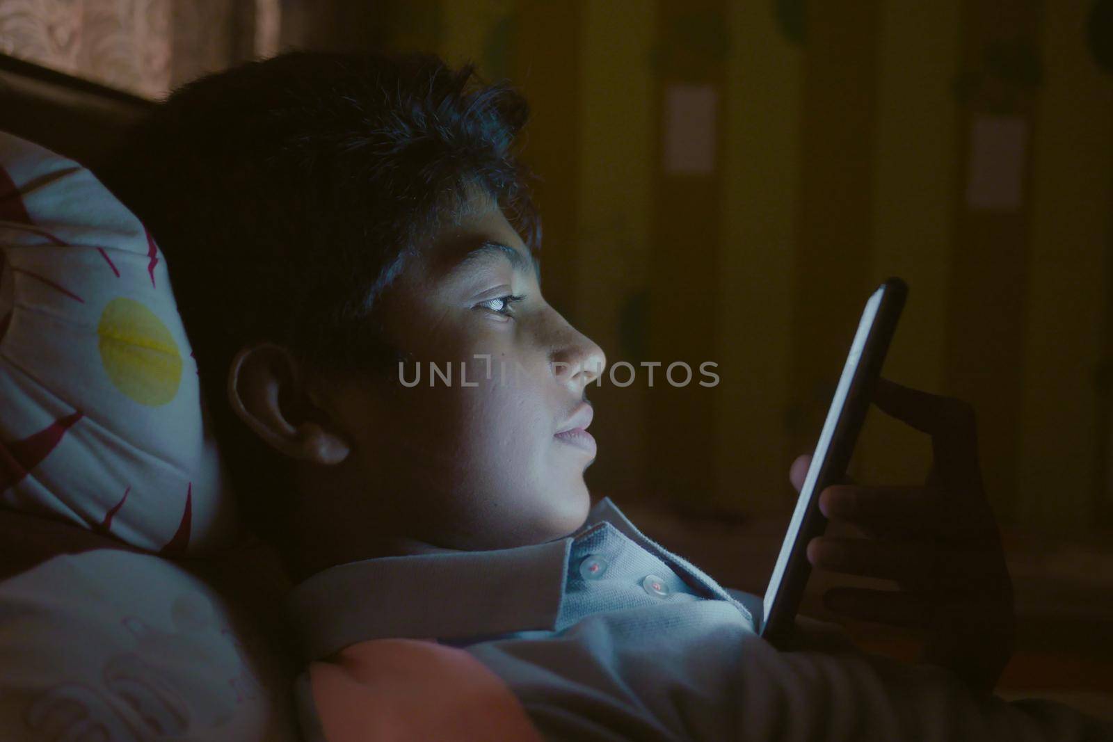 teenage boy sitting on sofa using smart phone at night .