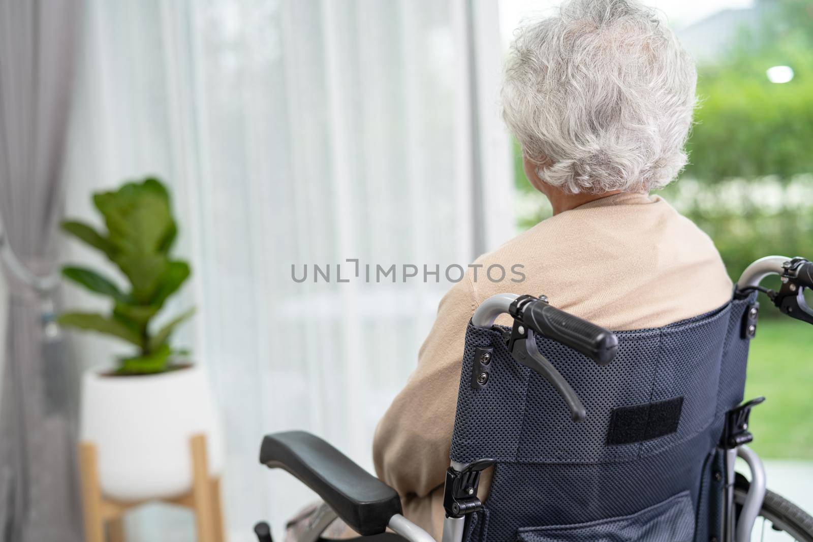 An elderly woman sitting on wheelchair looking out the window for waiting someone. Sadly, melancholy and depressed. by pamai