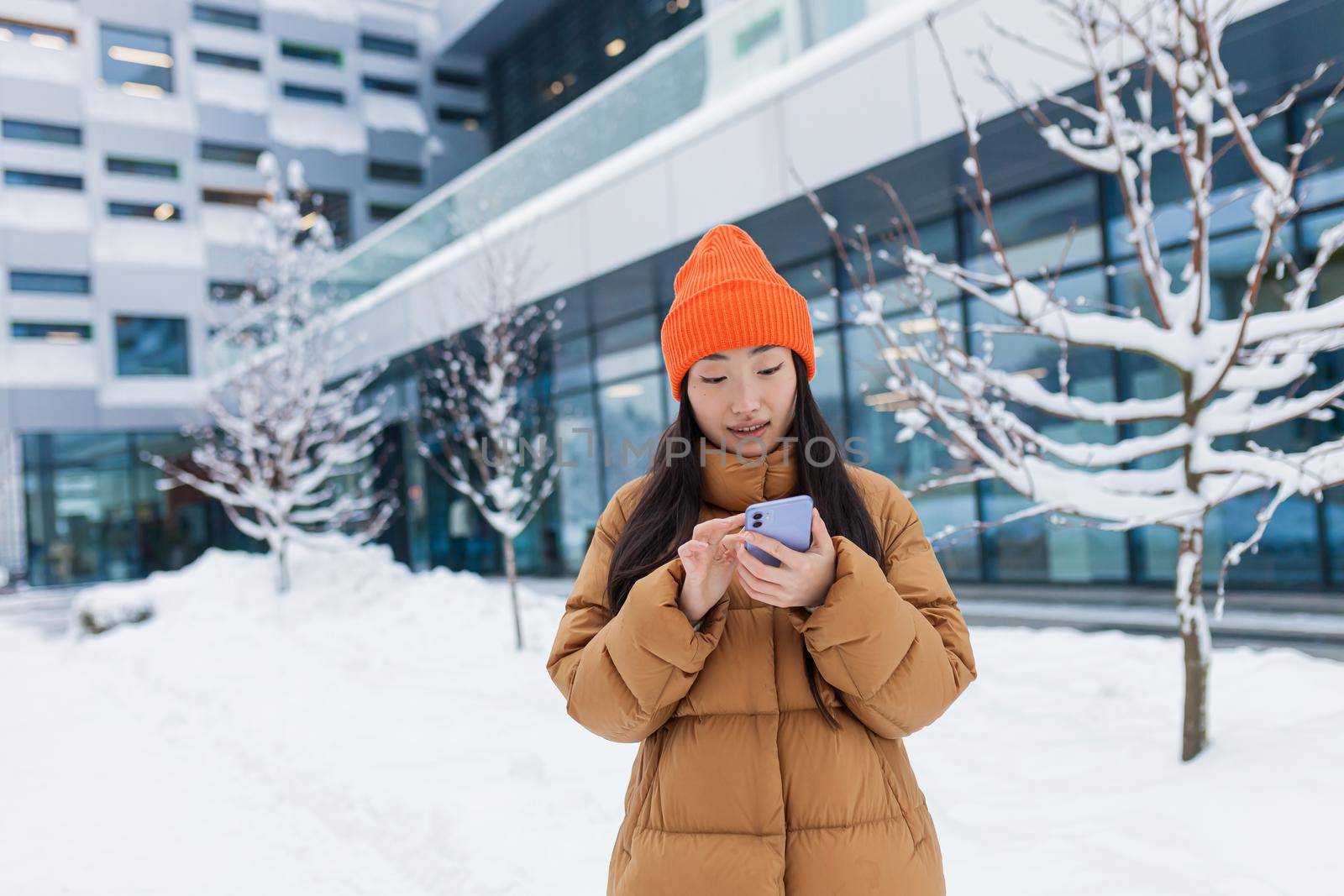 Beautiful Asian girl uses the phone, online dating, makes a choice, walks on a winter snowy day