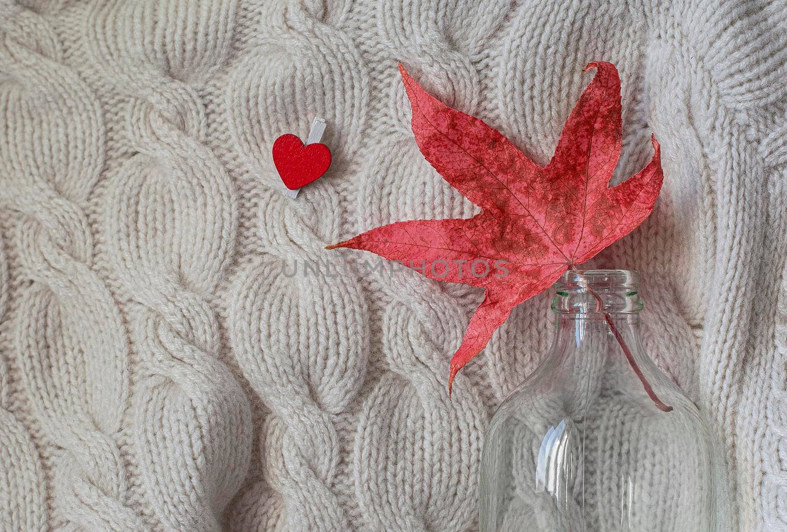 Hello autumn. Creative flat lay composition on light background. Red leaf, knitted sweater and small heart. Copy space.
