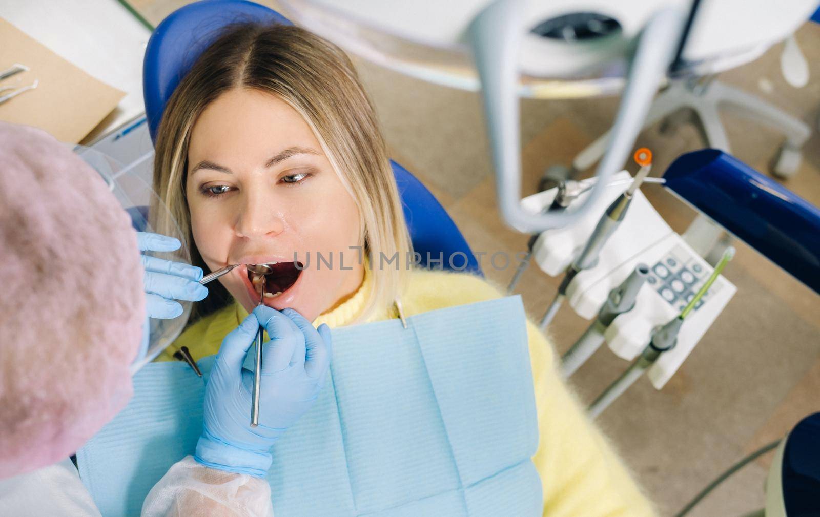 a dentist in a protective mask sits next to him and treats a patient in the dental office by Lobachad