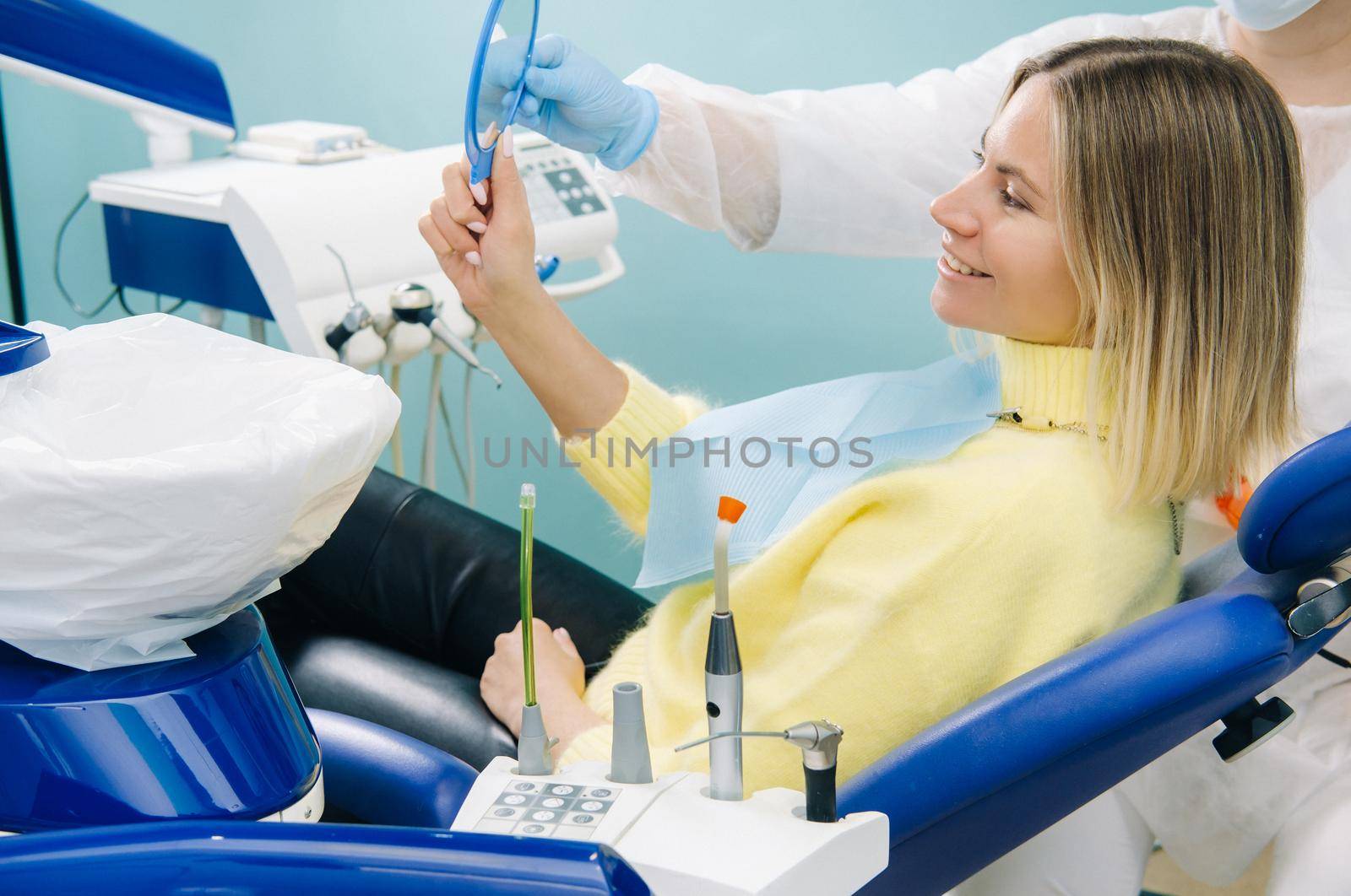 The girl smiles and looks in the mirror in dentistry by Lobachad