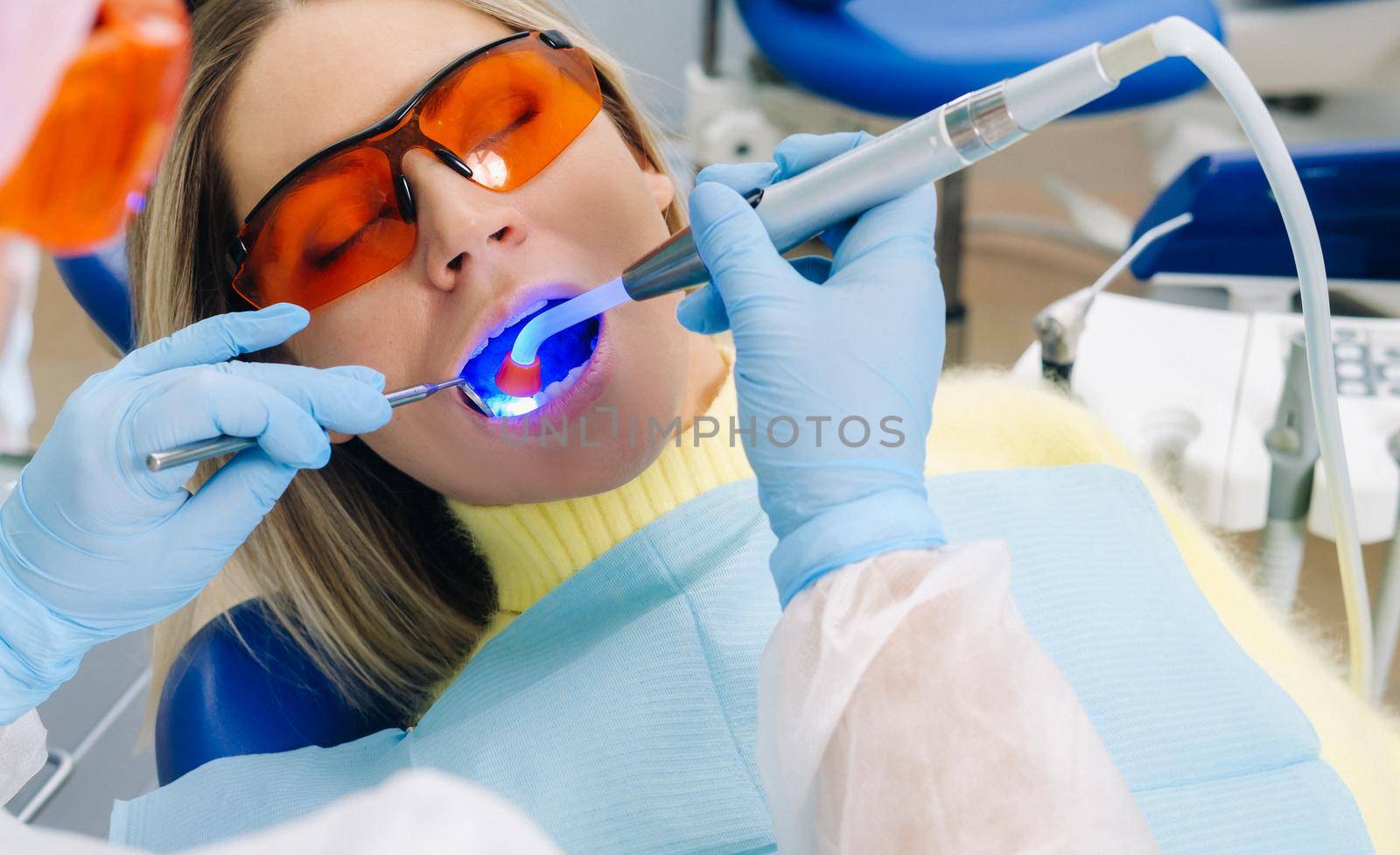 A young beautiful girl in dental glasses treats her teeth at the dentist with ultraviolet light. filling of teeth.