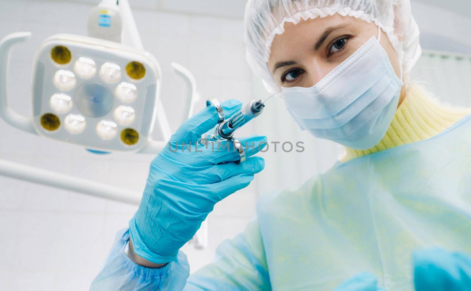 A masked dentist holds an injection syringe for a patient in the office.