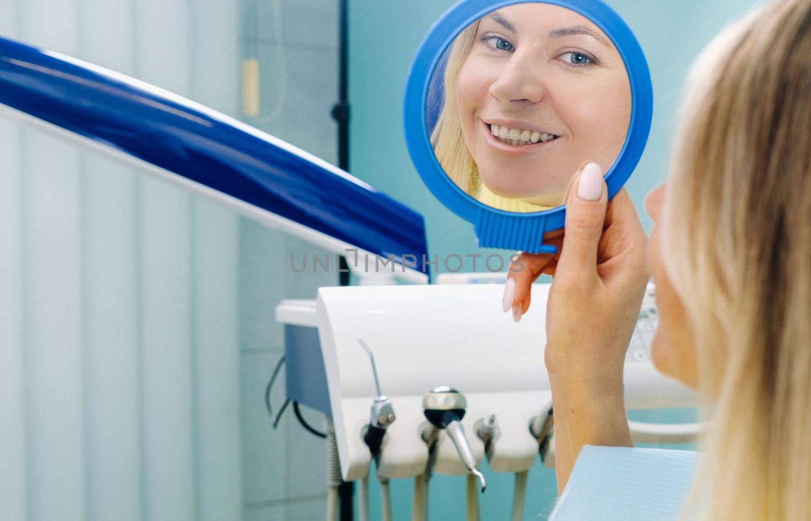 The girl smiles and looks in the mirror in dentistry by Lobachad