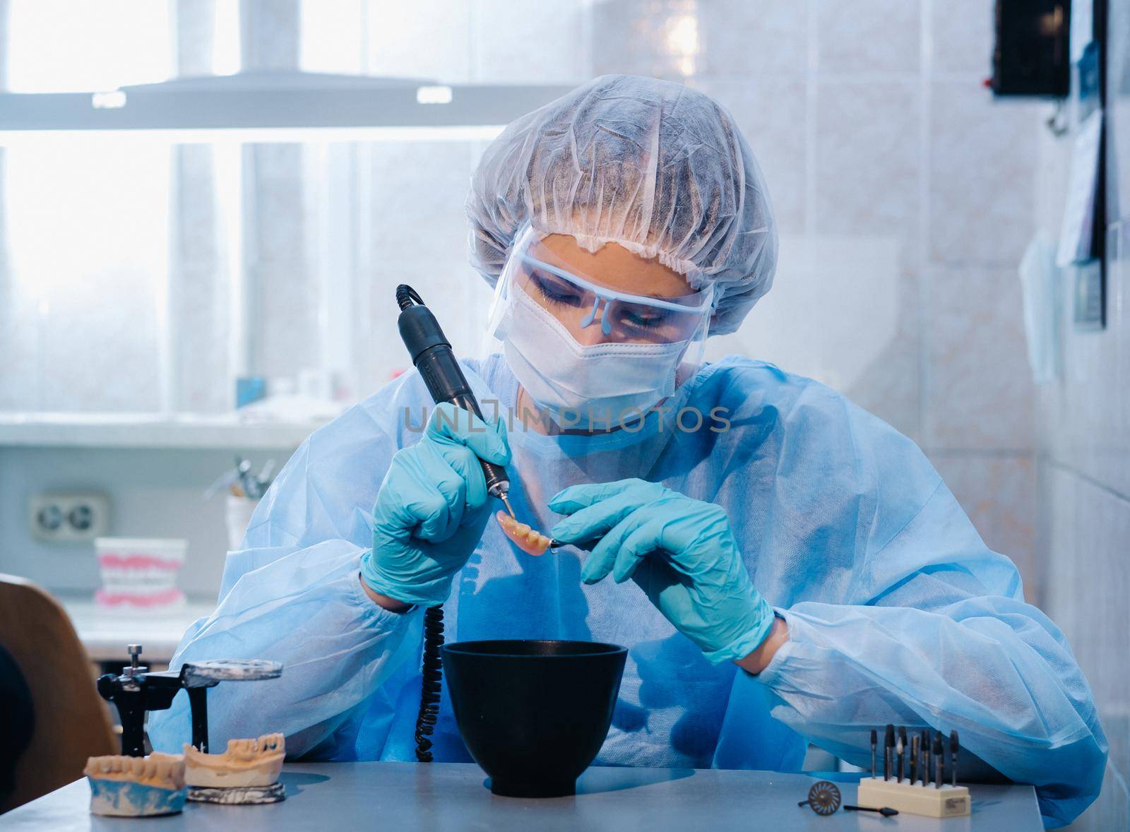 A dental technician in protective clothing is working on a prosthetic tooth in his laboratory by Lobachad