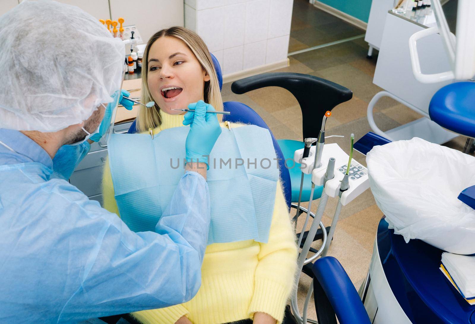 A male dentist with dental tools drills the teeth of a patient with an assistant. The concept of medicine, dentistry and healthcare.