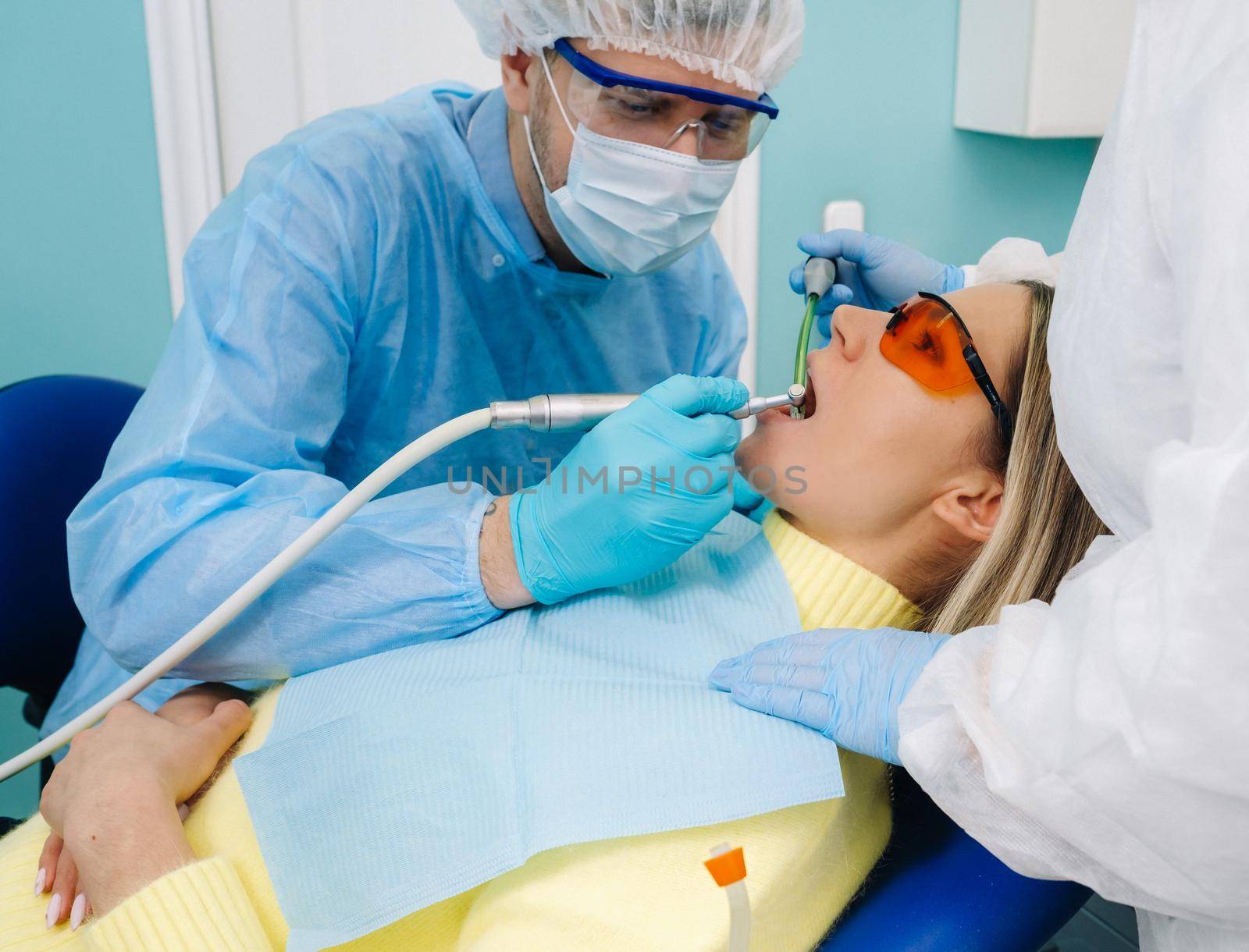 A male dentist with dental tools drills the teeth of a patient with an assistant. The concept of medicine, dentistry and healthcare by Lobachad
