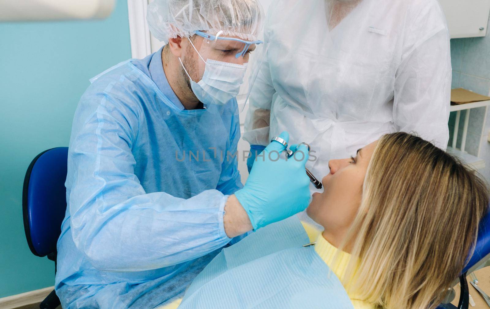 a dentist wearing a protective mask sits nearby and holds instruments in his hands before treating a patient in the dental office by Lobachad