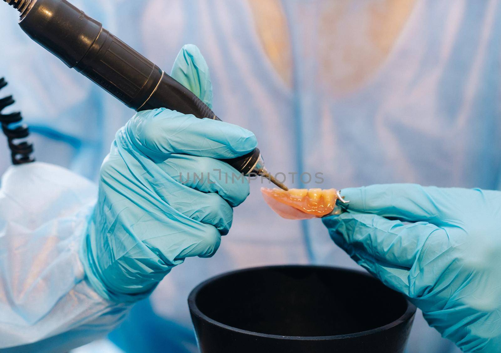 A masked and gloved dental technician works on a prosthetic tooth in his lab.