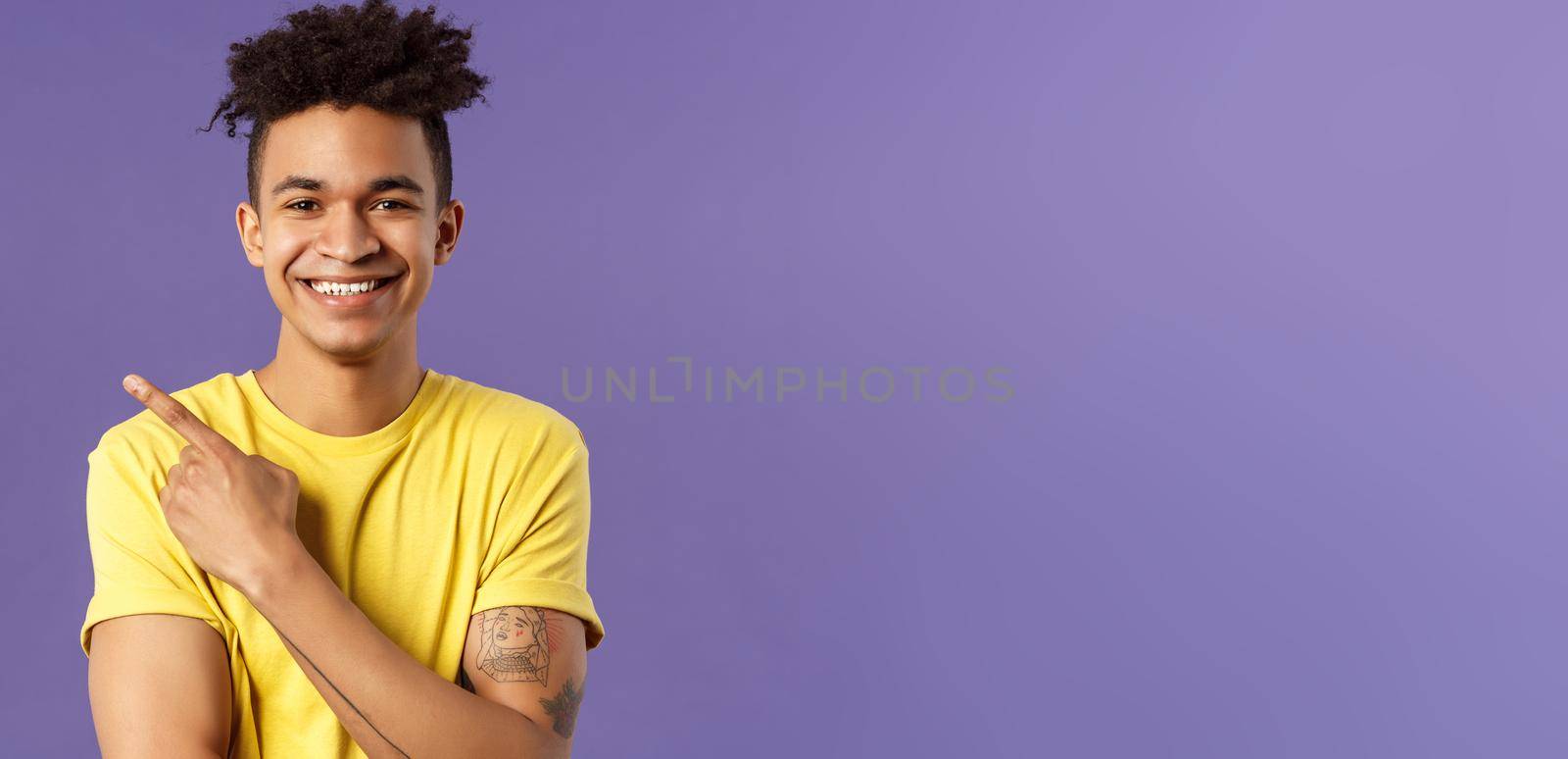 Close-up portrait of enthusiastic, happy young hipster male with dreads, beaming smile and pointing finger upper left corner, present cool product, introduce something really good, purple background.