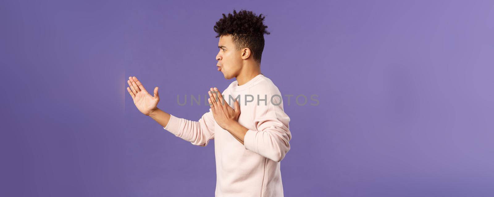 Profile portrait of young hispanic guy with dreads acting like he is ninja or martial arts fighter, practice his kung-fu or taekwondo skills, standing purple background. Copy space