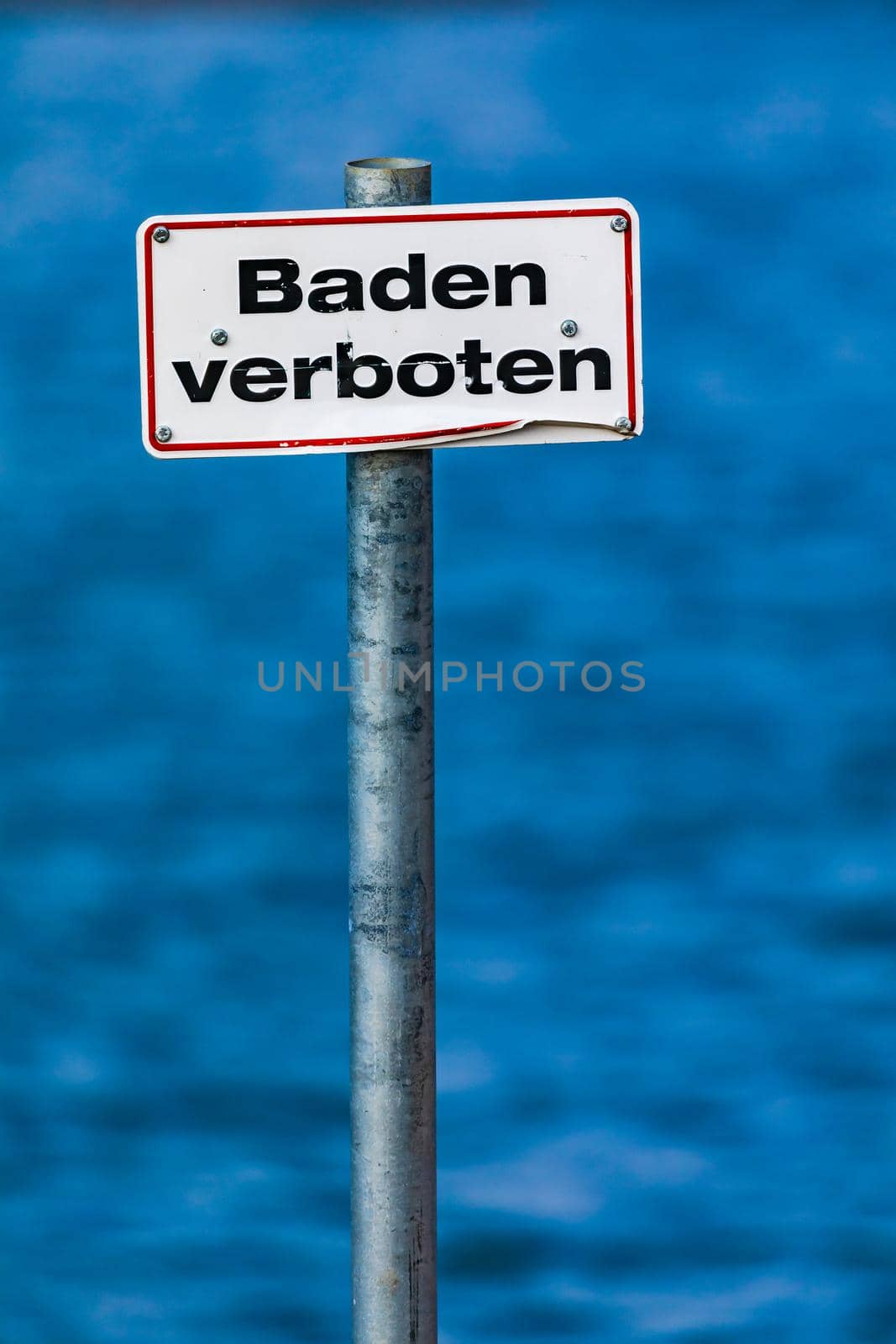 German no swimming sign on a pole isolated in front of a blue lake