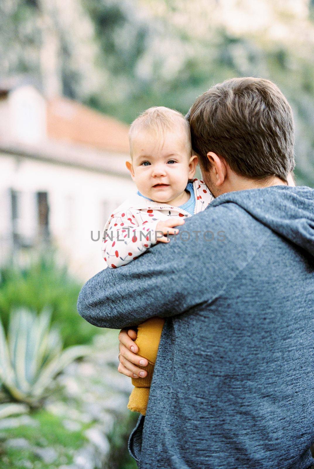 Baby peeks over the father shoulder. Portrait by Nadtochiy