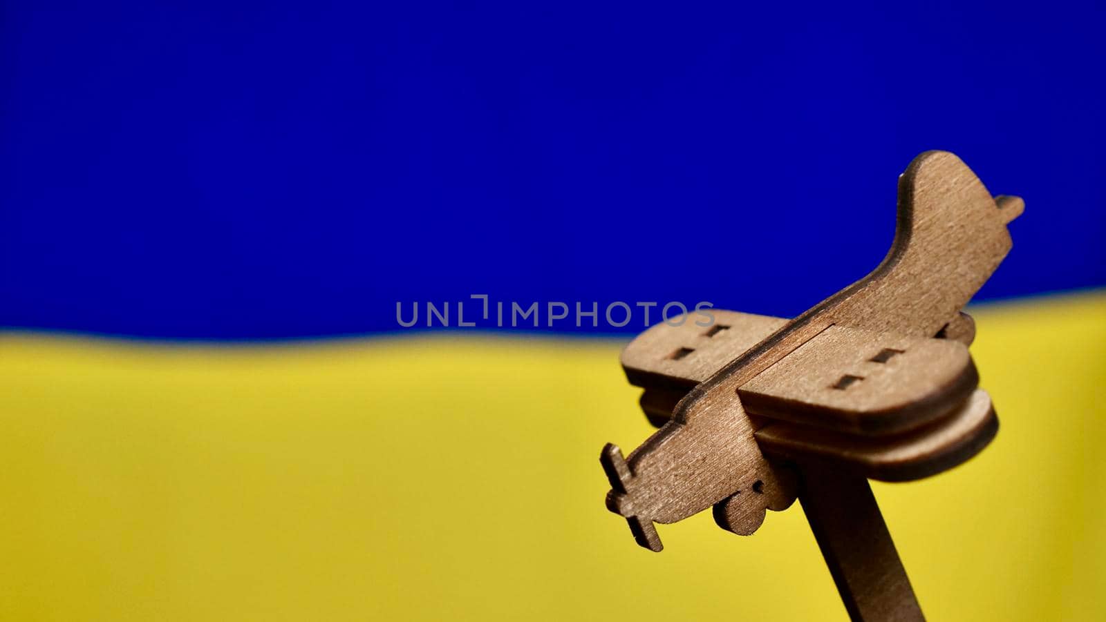 Decorative wooden toy plane on the yellow blue background of the Ukrainian flag. Russia attacked Ukraine in 2022