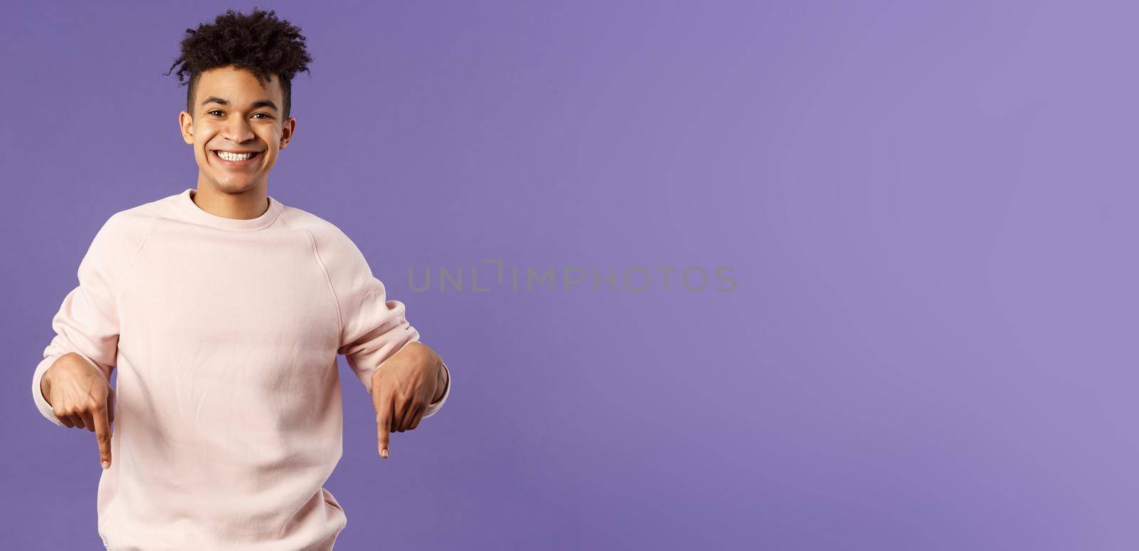 Portrait of cheerful, happy young 25s man recommending product, showing promo of product, delivery service, online shop or appllication, pointing fingers down, smiling pleased camera.