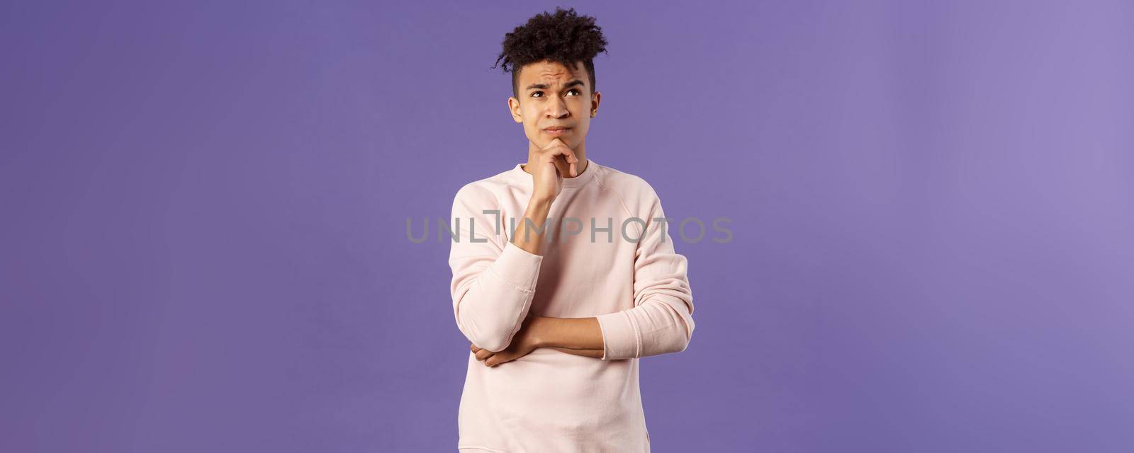 Portrait of complicated, young thoughtful man with dreads, look troubled up, thinking what to do, standing indecisive, grimacing not knowing answer, facing hard choices, purple background.