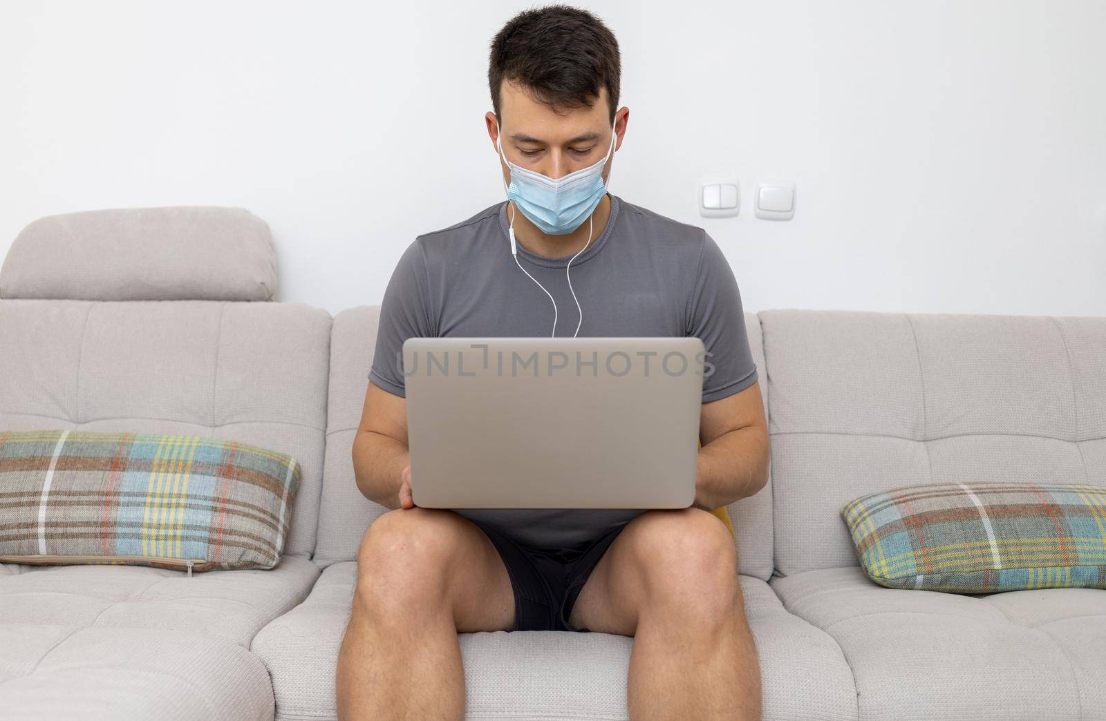 young man in mask and with laptop sitting on sofa. High quality photo