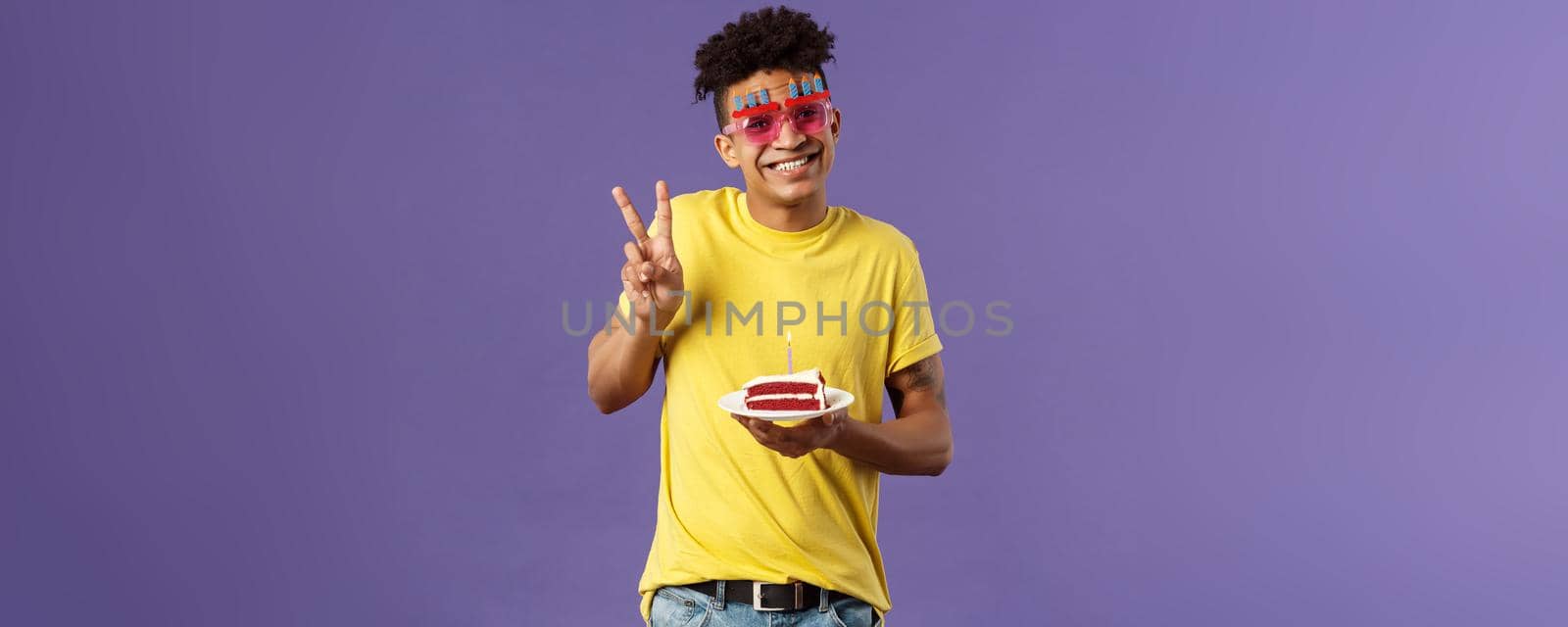 Celebration, party and holidays concept. Portrait of lovely charismatic hispaic guy in b-day glasses, celebrating his day, show peace sign photographing with birthday cake and lit candle, smiling.
