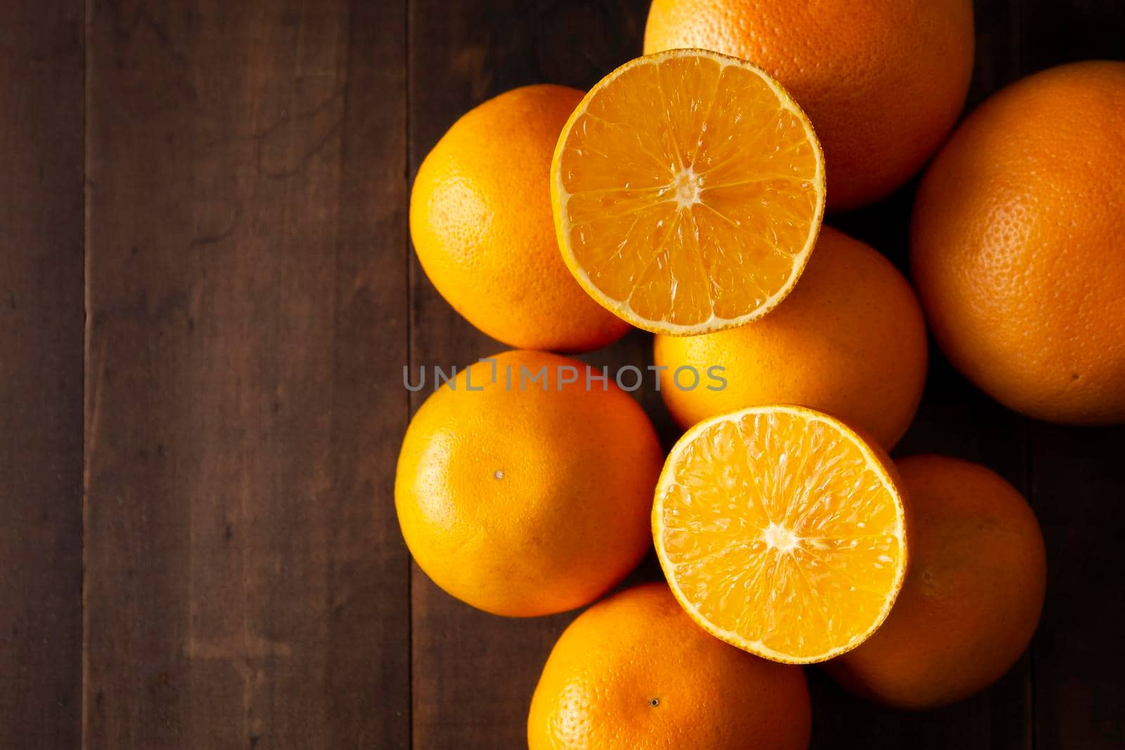 close up of a ripe orange cut in half and several whole oranges on brown rustic wooden table with copy space