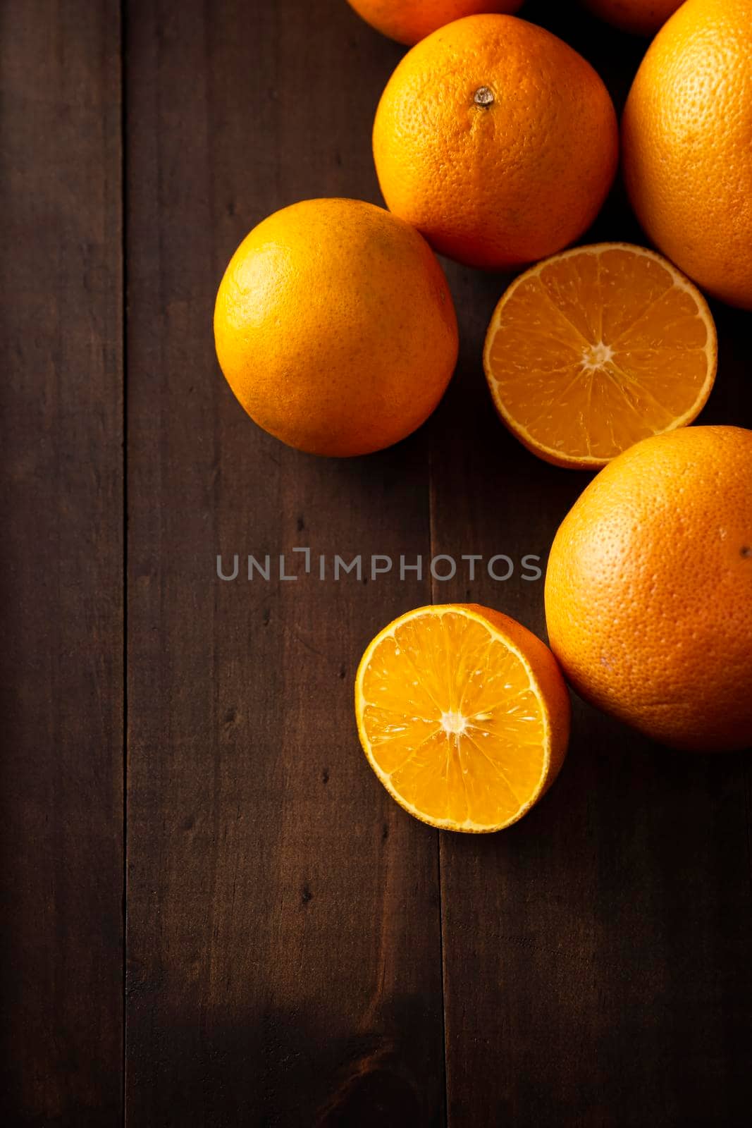 a ripe orange cut in half and several whole oranges on brown rustic wooden table with copy space