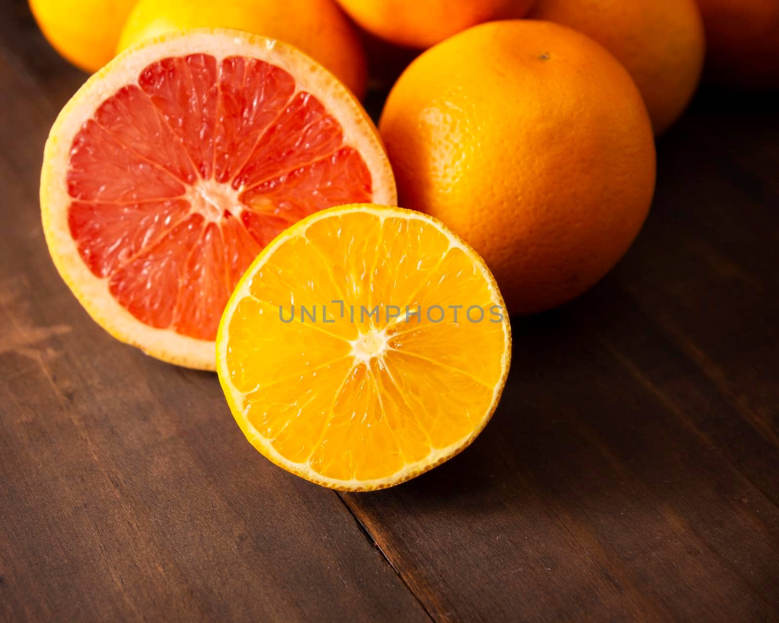 close up of ripe orange and grapefruit slices and several whole oranges on brown rustic wooden table with copy space
