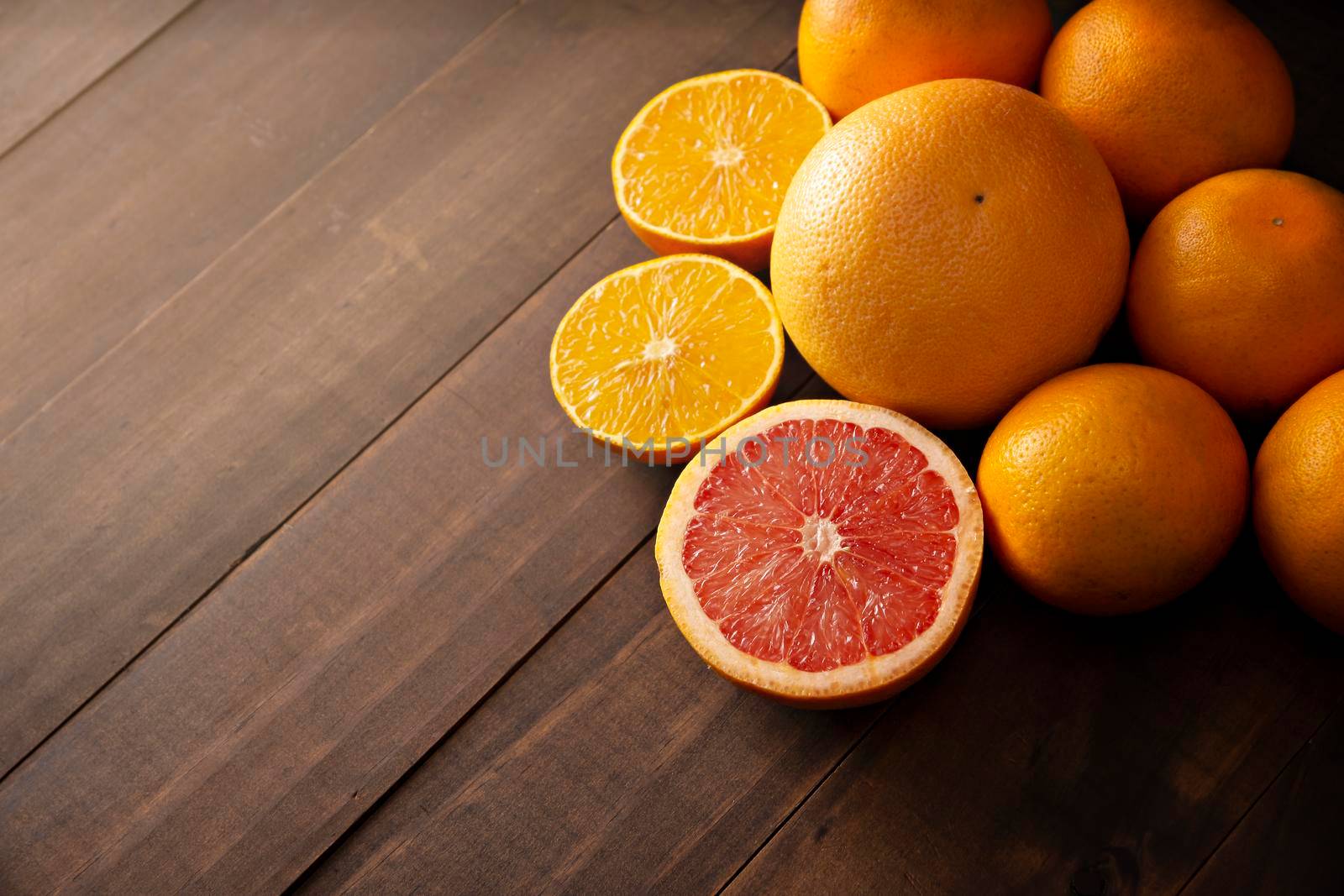 ripe orange and grapefruit slices and several whole oranges on brown rustic wooden table with copy space