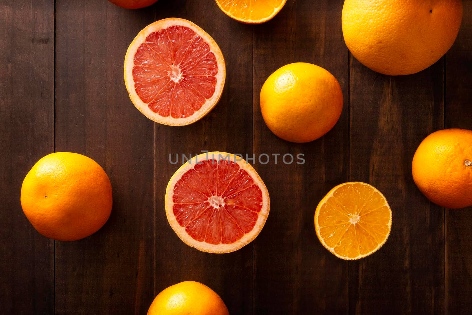 top view image of ripe orange and grapefruit slices and several whole oranges on brown rustic wooden table