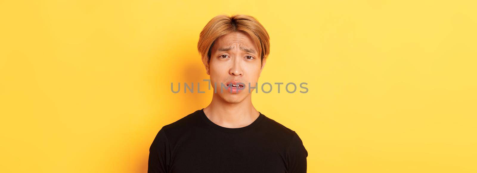 Close-up of confused and upset asian blond guy looking puzzled, open mouth and frowning perplexed, standing over yellow background by Benzoix