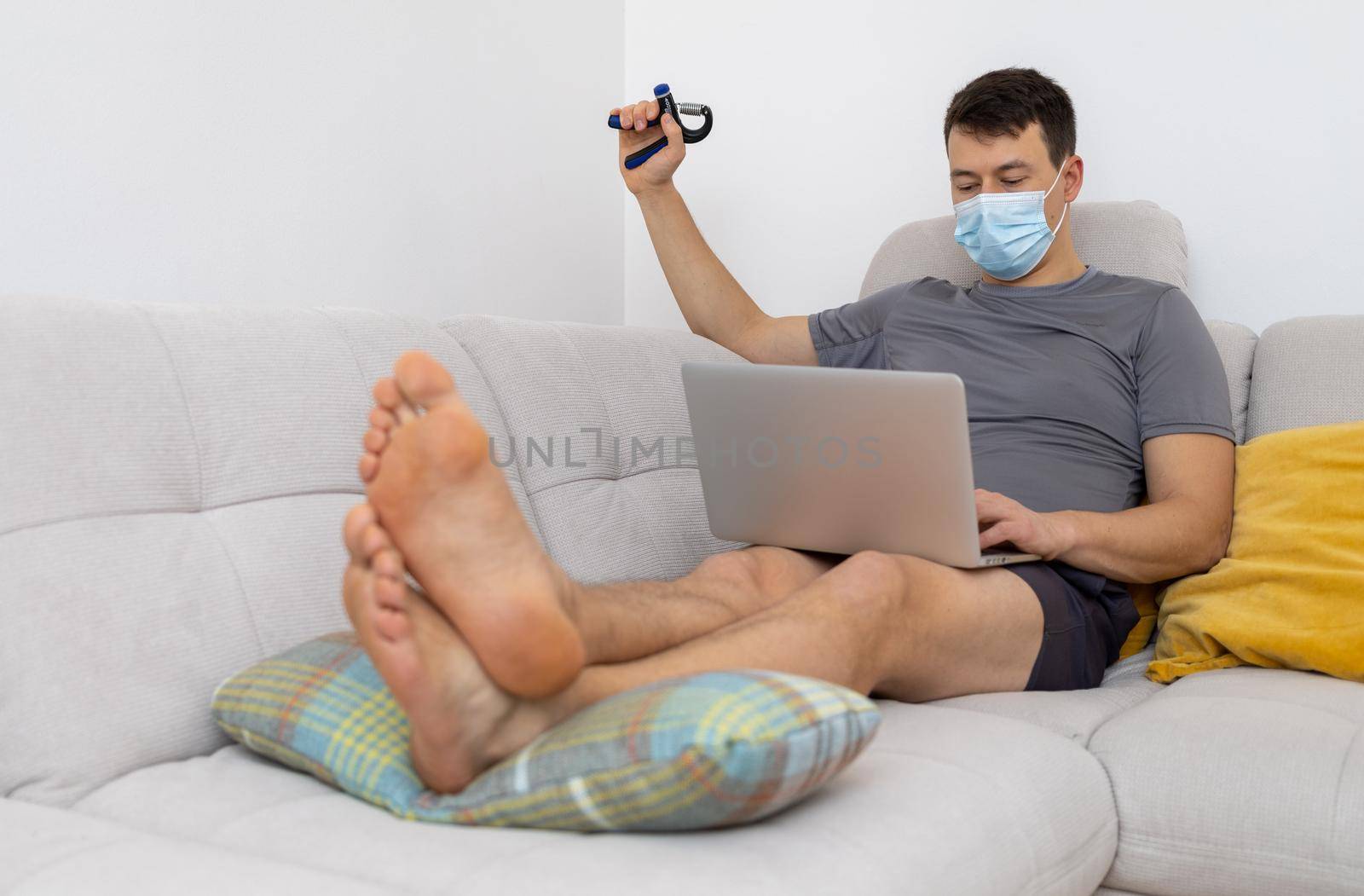 young man in mask and with laptop sitting on sofa. High quality photo