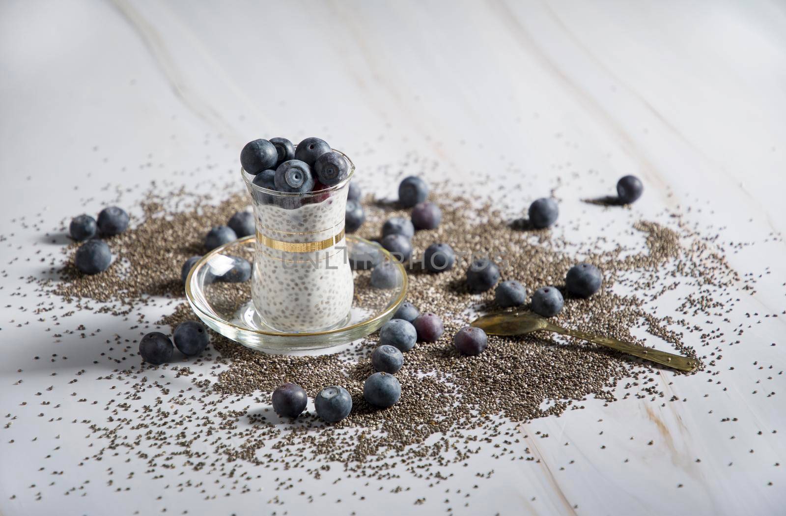 dessert of chia seeds, yogurt and blueberries in a glass transparent glass on a light background where seeds and berries are scattered, High qualitu photo