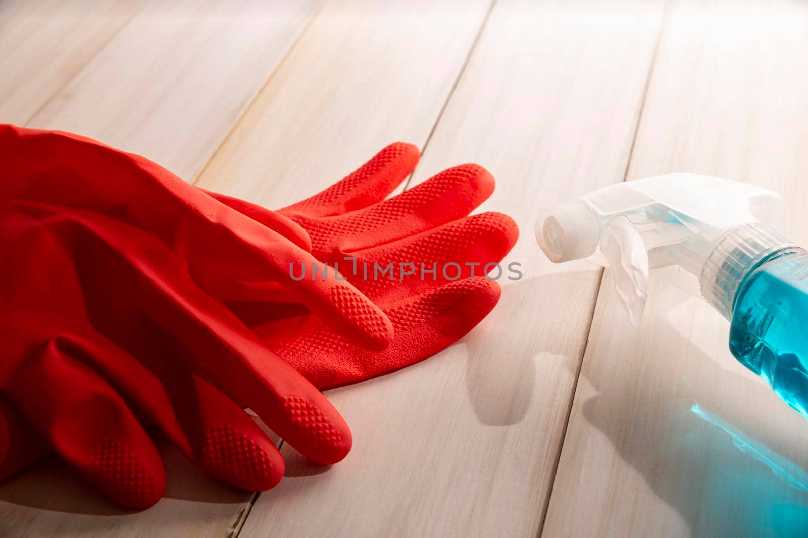 red rubber gloves and liquid detergent in sparay bottle on wooden background, cleaning and sanitization concept