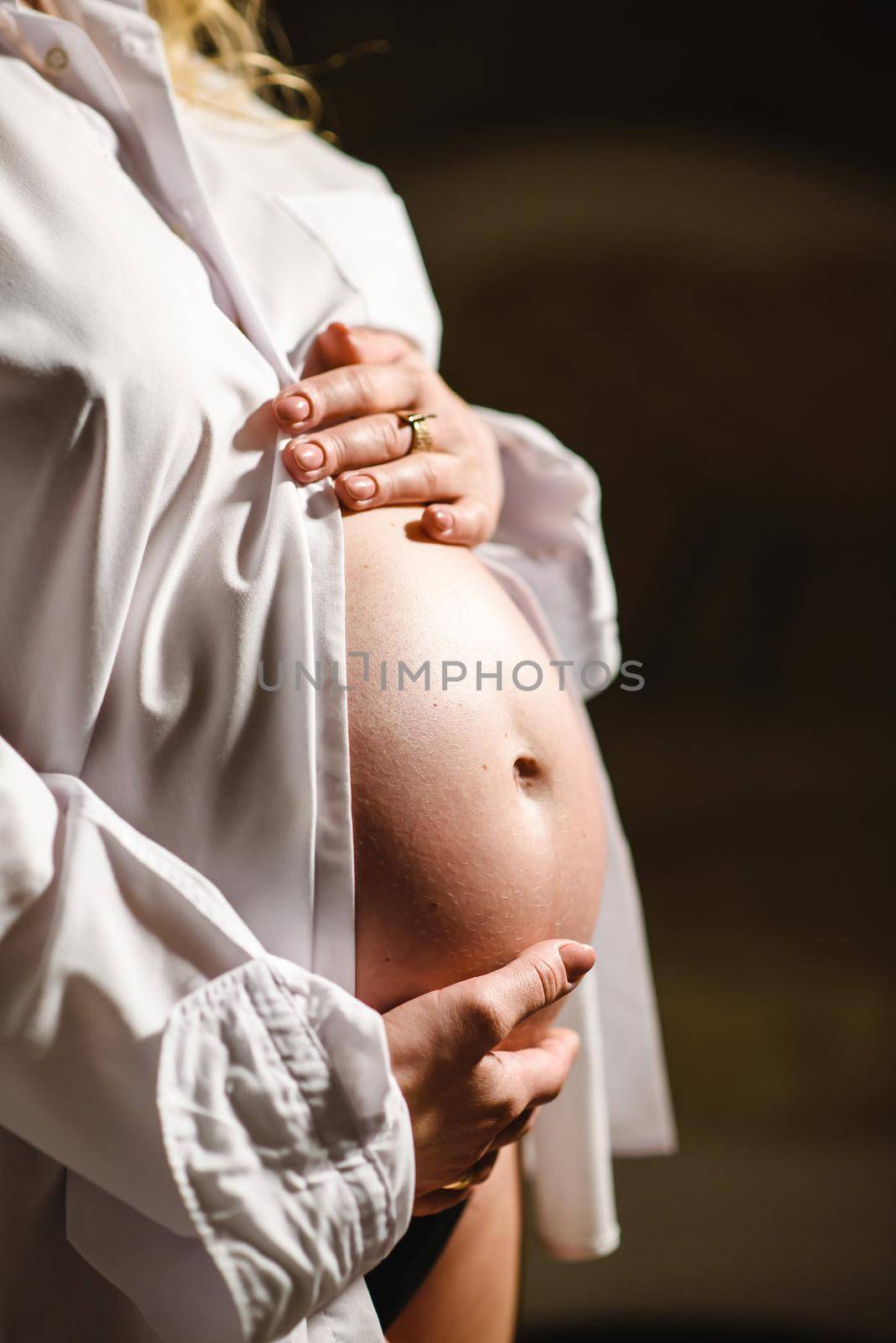 Pregnant woman in white shirt, holding belly with hands