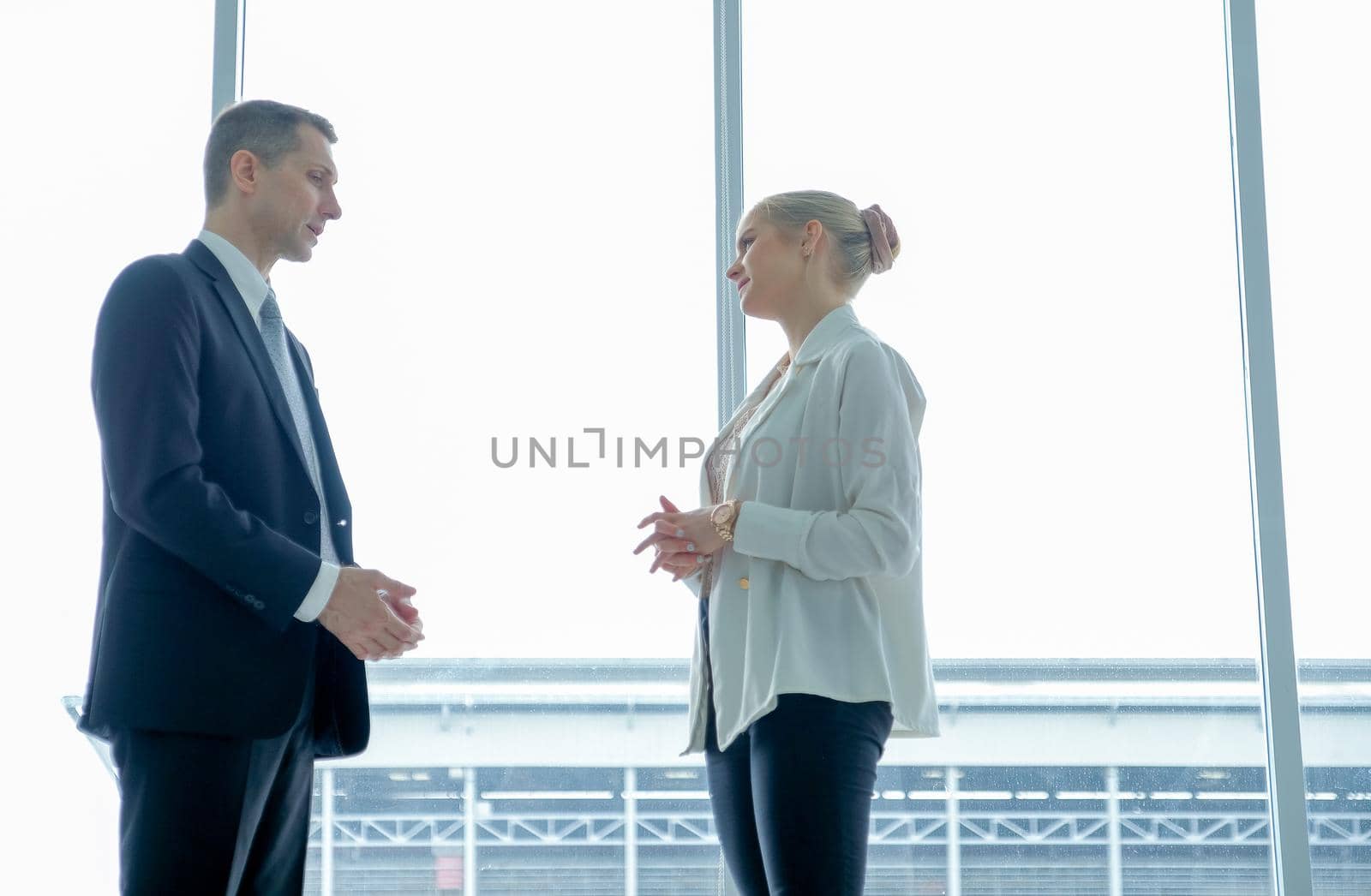 Business man and woman talk together in front of grass windows with day light.