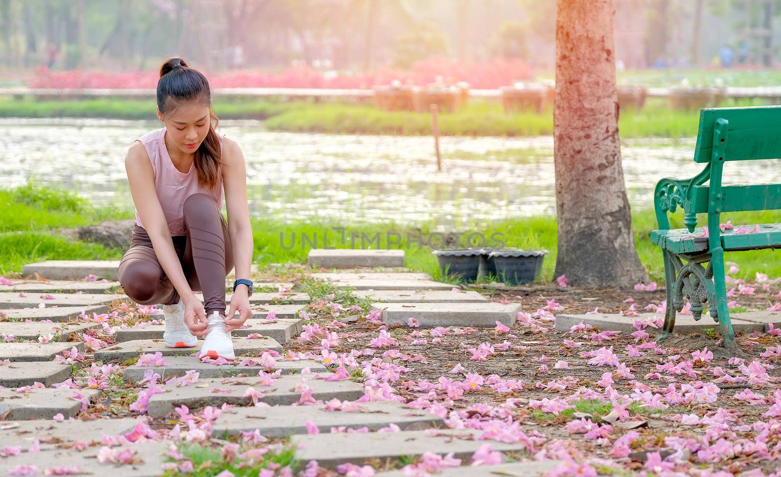 Portrait of beautiful sport girl is tying shoelace on bricks and pink flower spread to the floor in the garden with morning light.