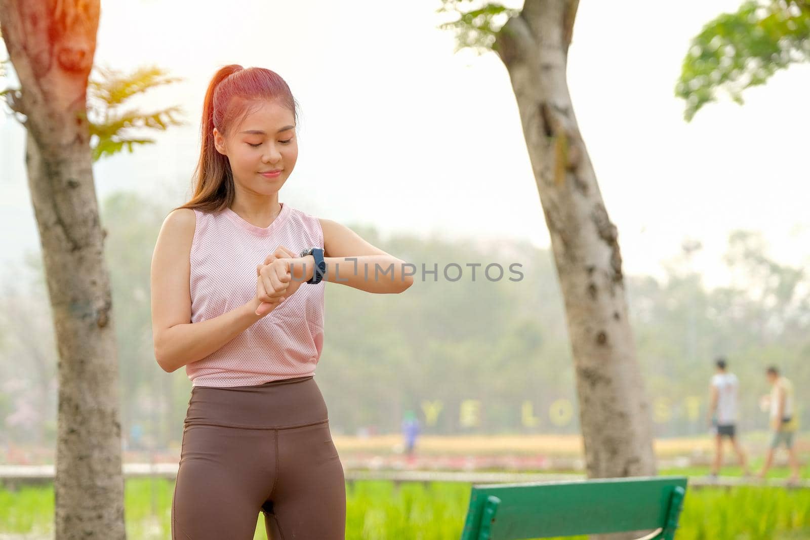 Portrait of young beautiful sport girl look to her watch and stay in park or garden with morning light.
