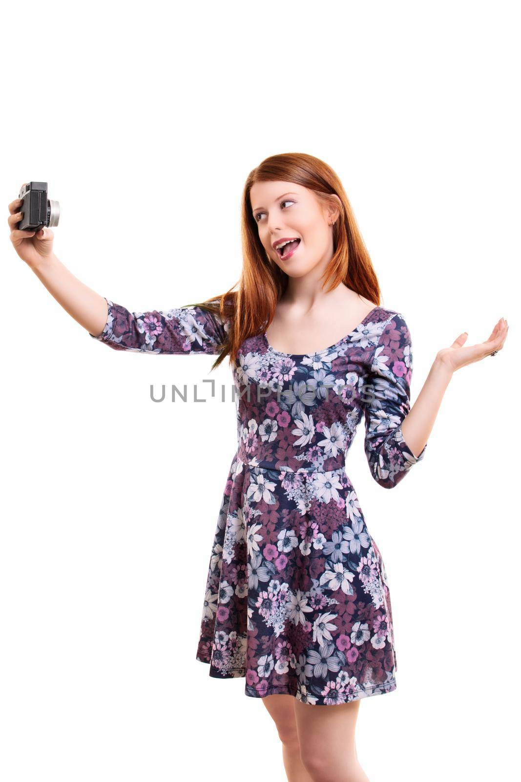 Beautiful young woman in a flowery dress taking a selfie or filming her self, isolated on white background. Attractive redhead girl with long hair vlogging. Lifestyle, happiness, and social concept.