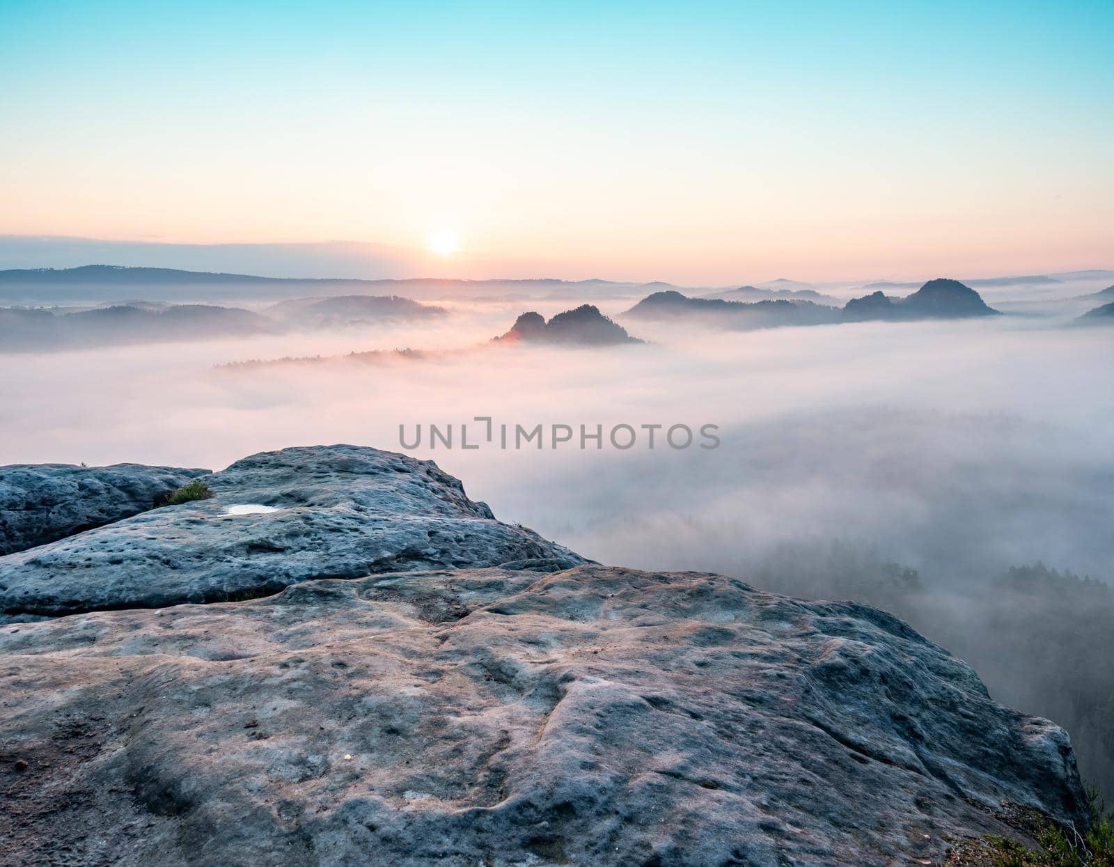 Mountain top rock, sleepy misty landscape bellow under heavy morning  fog