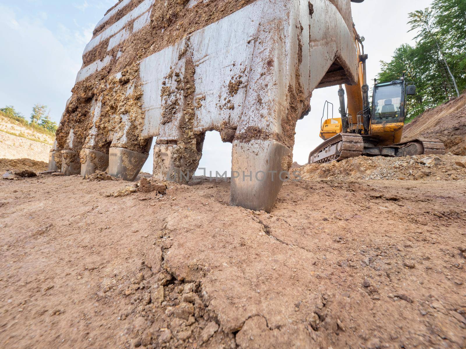 Large loader bucket with sharp teeth. Industrial track type excavator digging at a quarry. 