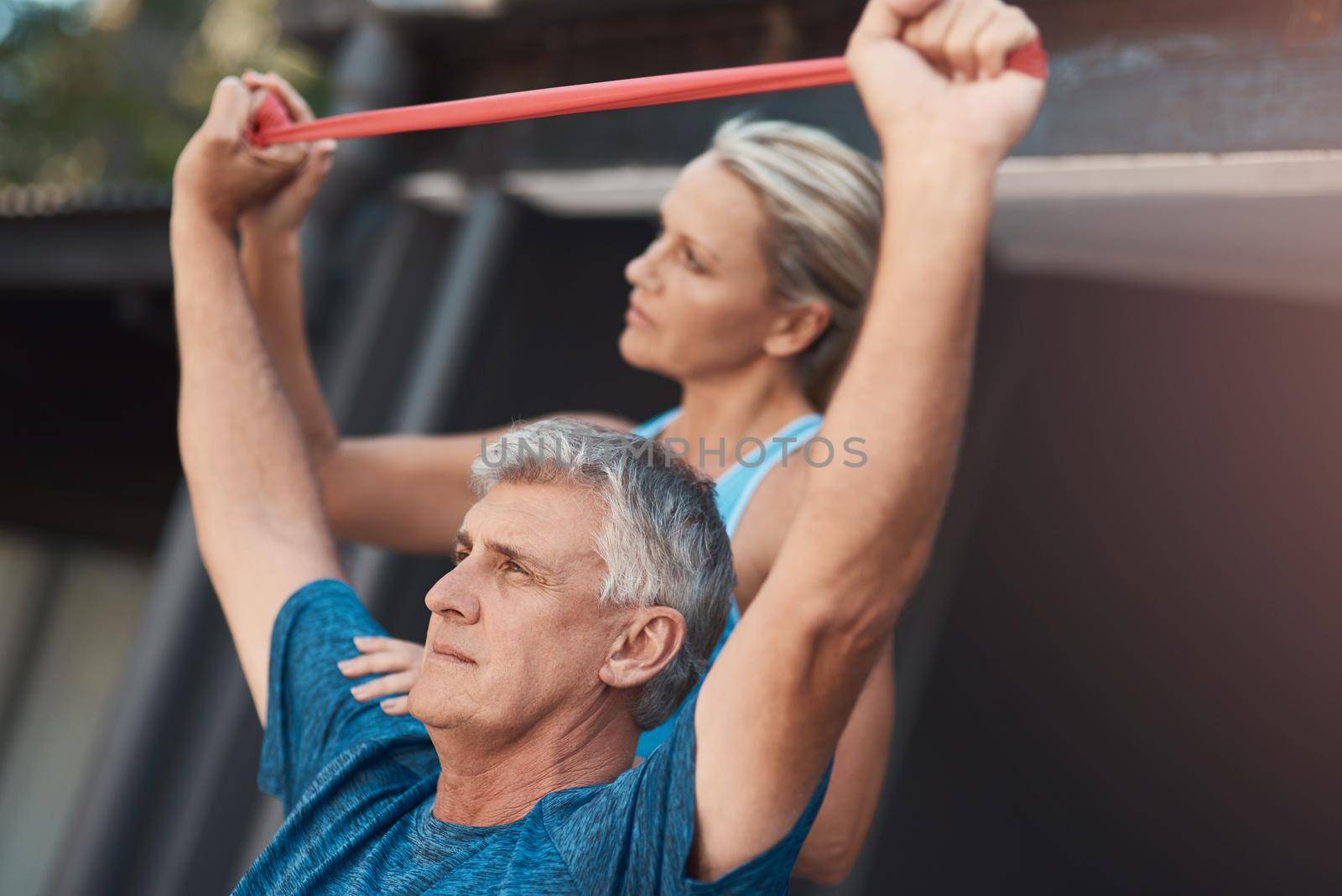 Stay motivated no matter what. a mature man stretching his arm muscles with an elastic band while being assisted by a woman. by YuriArcurs