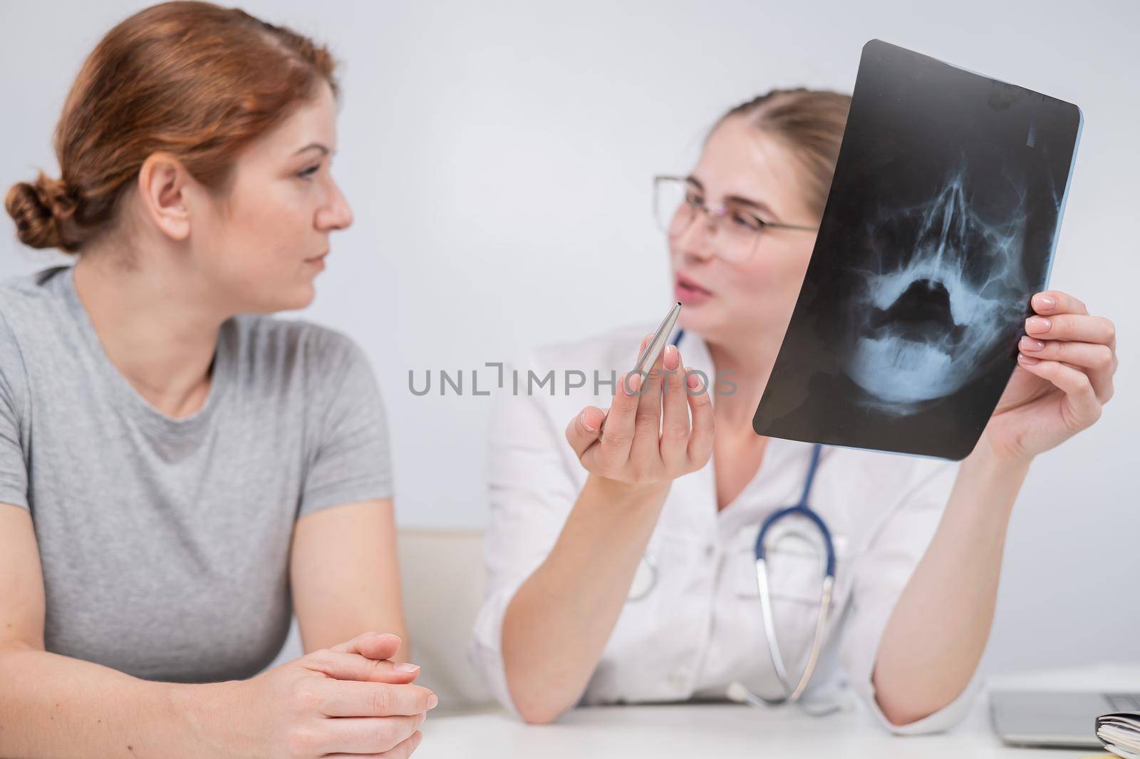 A woman doctor and a patient at the reception are discussing an x-ray of the sinuses