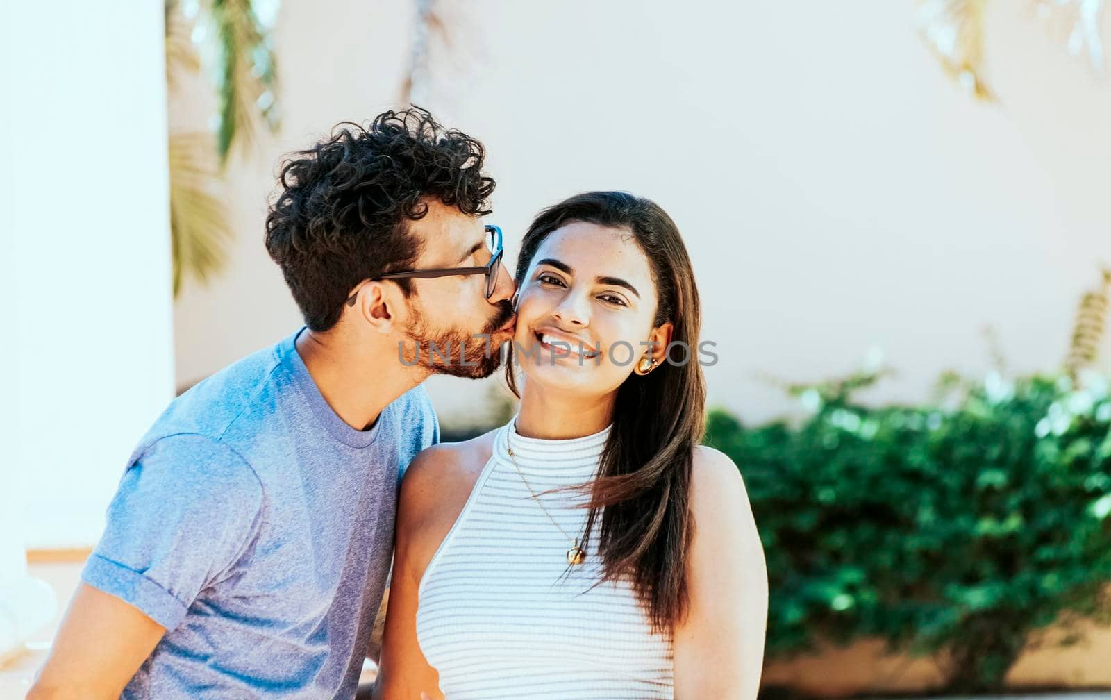 Boyfriend kissing his girlfriend on the cheek while smiling. Young man kissing his girlfriend on the cheek while smiling. Guy kissing his girlfriend cheek and she smiles by isaiphoto