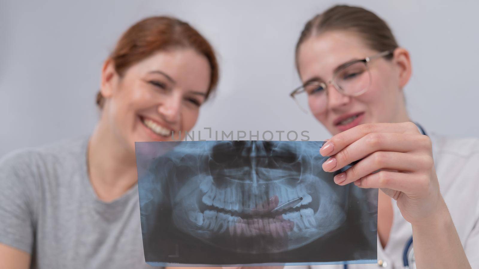 A woman doctor and a patient at the reception are discussing an x-ray of the jaw